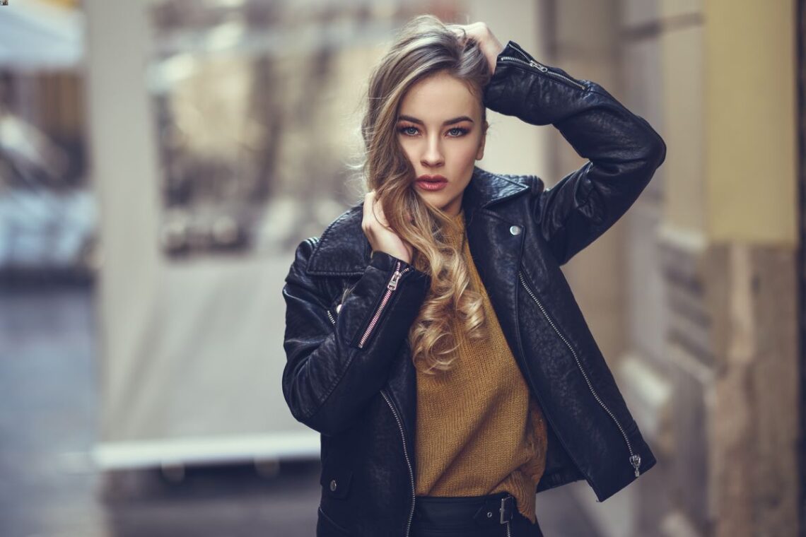 Jolie jeune femme portant un perfecto en cuir et se touchant les cheveux dans la rue