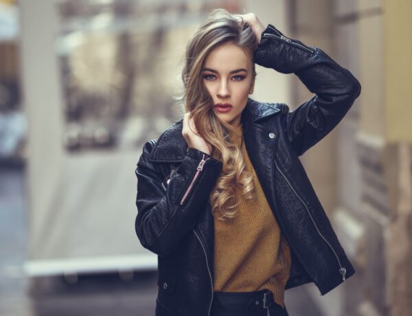 Jolie jeune femme portant un perfecto en cuir et se touchant les cheveux dans la rue