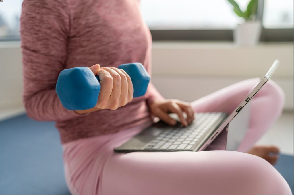 Jeune femme faisant du sport en télétravail en tenant un ordinateur